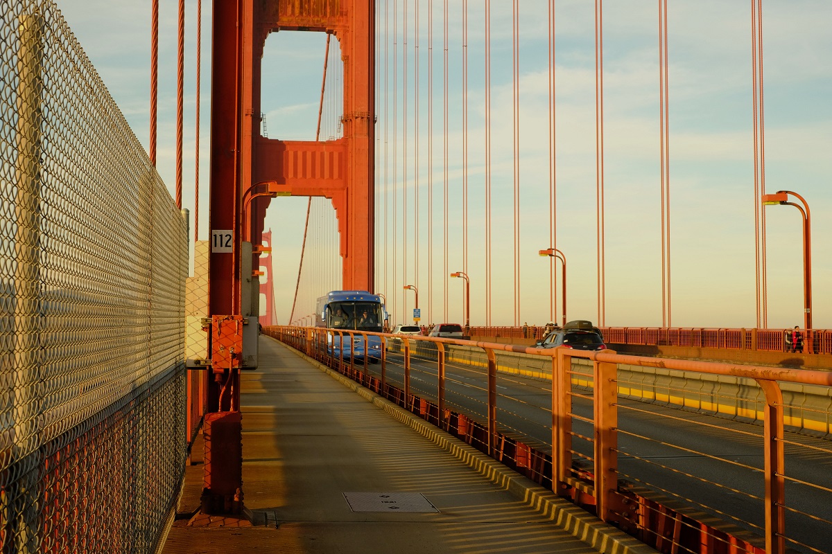 A bus drives in the sunshine on Golden Gate-bron in San Francisco. Cars and pedestrians on the bridge can also be seen in the background.